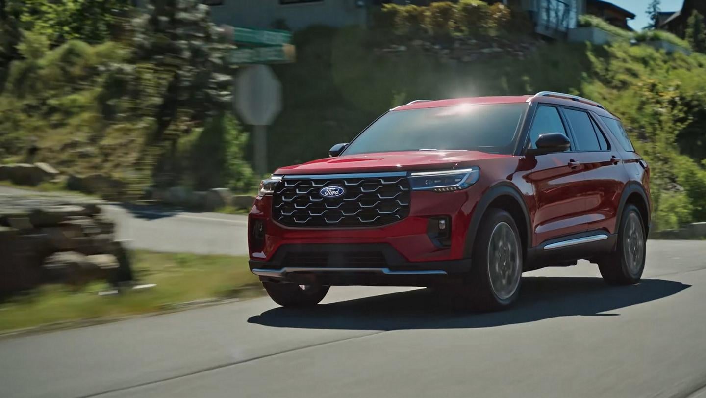 Red 2027 Ford Explorer driving through a mountain community.