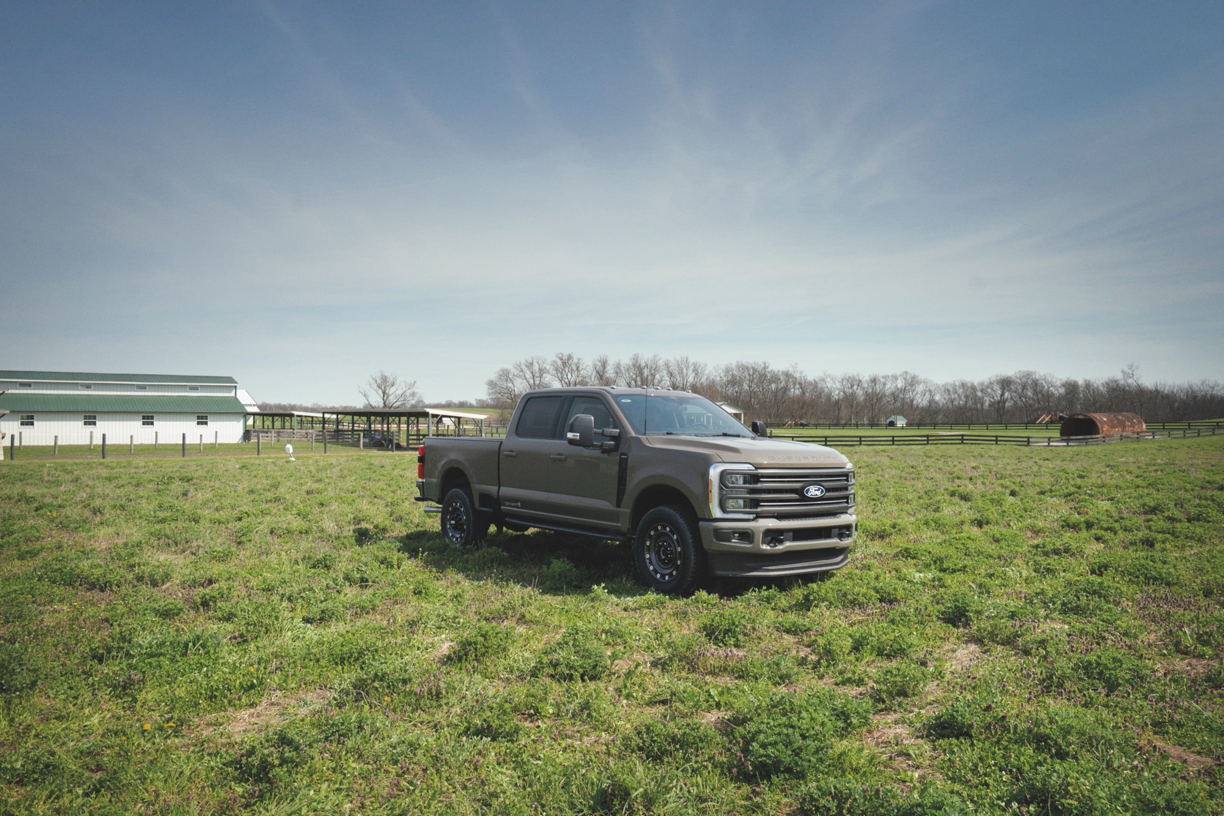 2027 Ford F-250 Super Duty parked in a green field near a working farm.